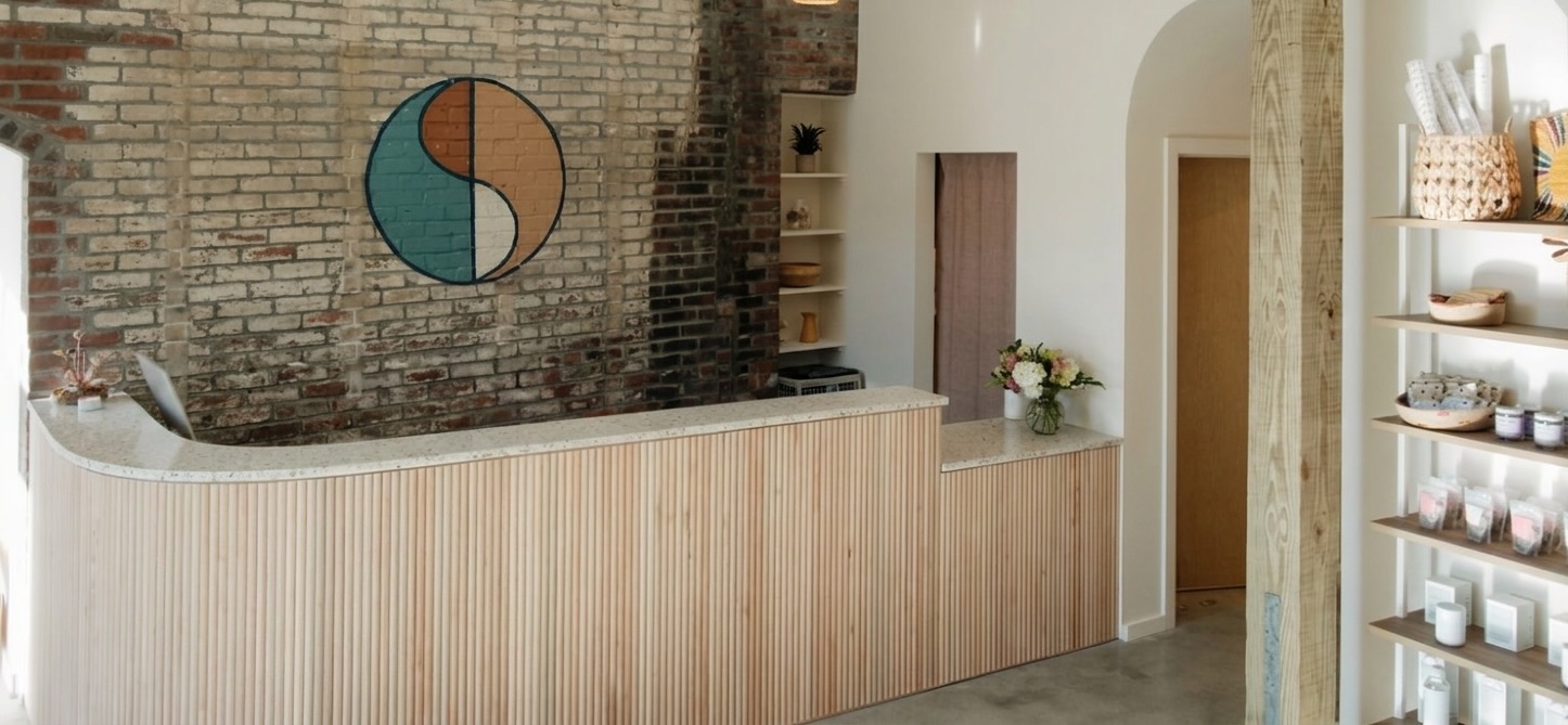 Skin Shaman reception — reclaimed brick wall with the Skin Shaman mark behind a curved wood-paneled front desk